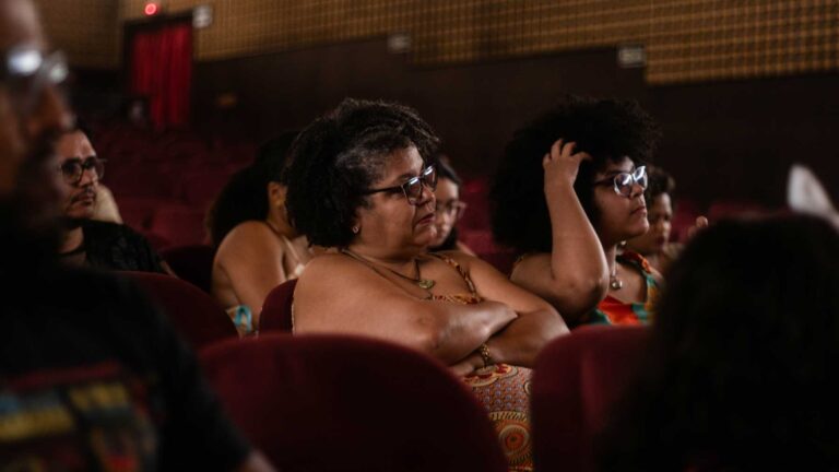 Mulher de braços cruzados prestando atenção na palestra