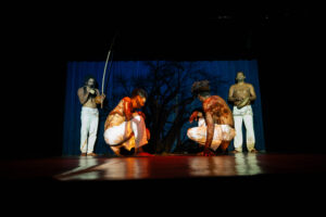 Pessoas jogam capoeira com berimbau e pandeiro